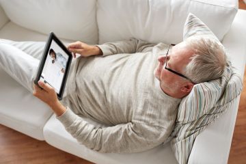 Ein Mann liegt auf einem Sofa und schaut auf sein Tablet