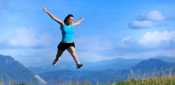Eine Frau springt in die Luft, im Hintergrund sieht man die Berge