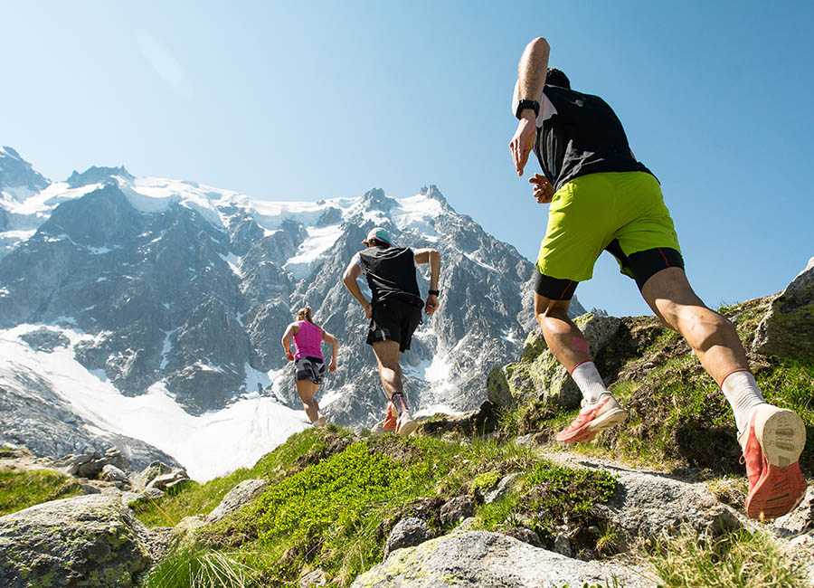 3 Personen in Laufsachen rennen auf einen Wanderweg in den Bergen